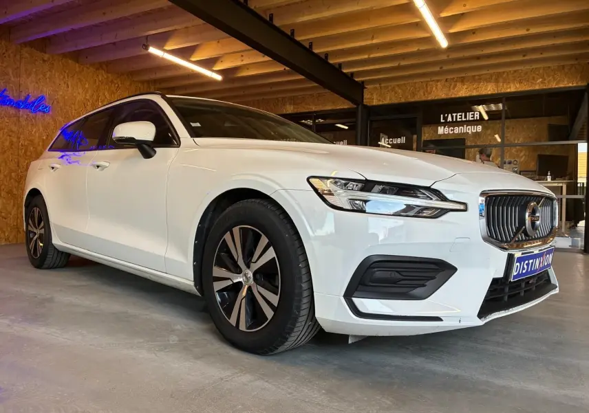 Volvo V60 D3 blanche vue en 3/4 avant droit, avec calandre chromée et jantes bi-ton dans un garage.