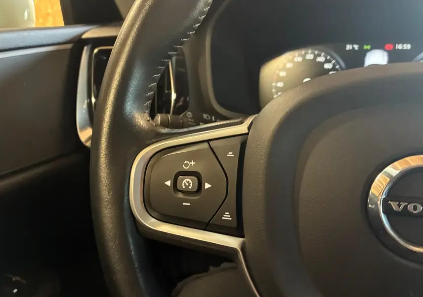 Gros plan sur le volant côté gauche d’un Volvo V60 blanc, montrant les commandes de régulateur de vitesse et le tableau de bord flou.