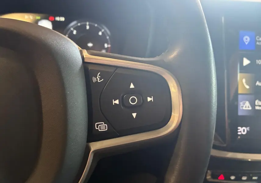 Gros plan sur les commandes au volant côté gauche d’un Volvo V60 blanc, avec tableau de bord et écran tactile en arrière-plan.