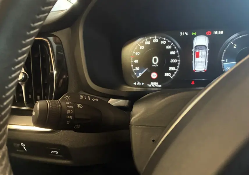 Vue rapprochée du combiné d'instruments et du commodo d'éclairage noir dans le tableau de bord d'une Volvo V60 blanche.