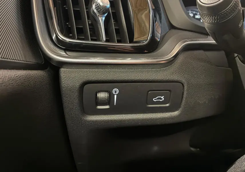Détail intérieur côté gauche du tableau de bord de la Volvo V60 blanche, avec commande d'éclairage et bouton ouverture coffre.