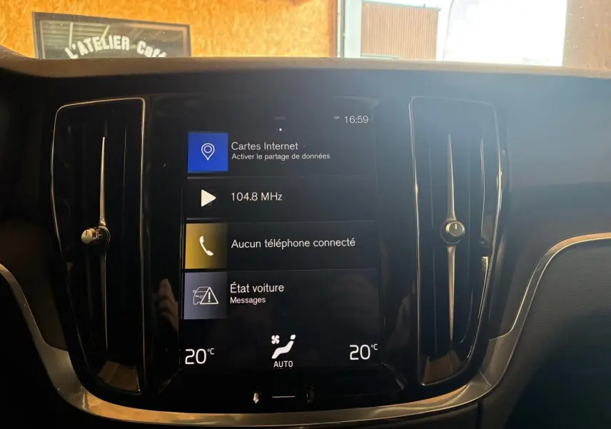 Vue rapprochée de l’écran tactile central noir du tableau de bord du Volvo V60 blanc, affichant la climatisation et la radio.