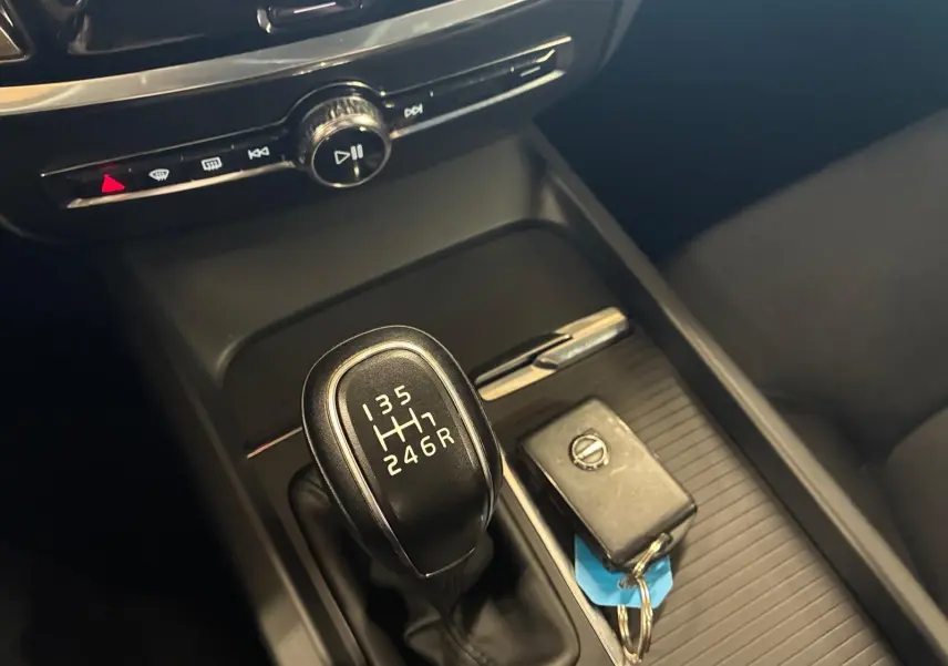 Gros plan sur la console centrale noire d’un Volvo V60 blanc, mettant en valeur le levier de vitesse manuel et une clé Volvo posée à côté.