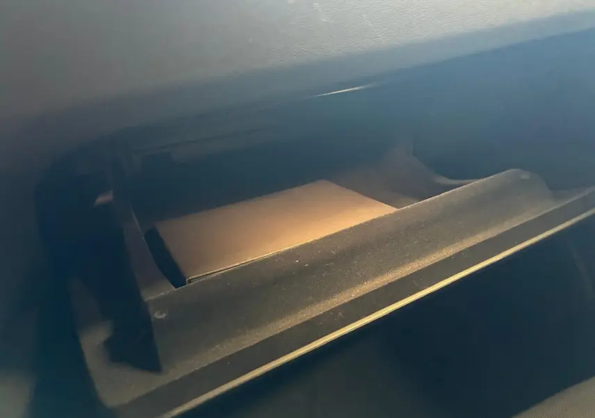 Gros plan sur la boîte à gants ouverte de la Volvo V60 D3 2020, intérieur noir avec un manuel visible.