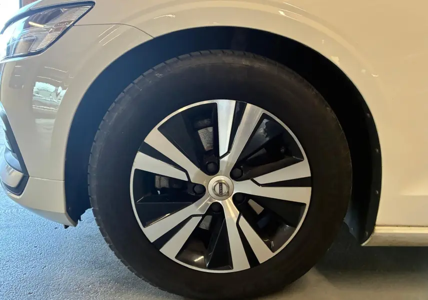 Gros plan sur la roue avant gauche d’un Volvo V60 blanc, mettant en valeur la jante bicolore moderne.