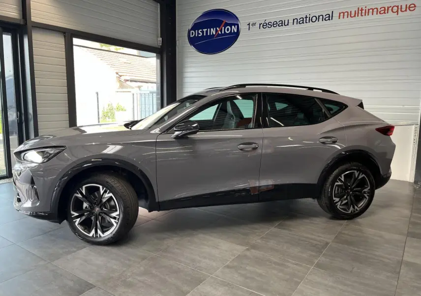 Vue de profil côté gauche du CUPRA Formentor gris clair 2025 avec jantes alliage noires et toit ouvrant panoramique en showroom.