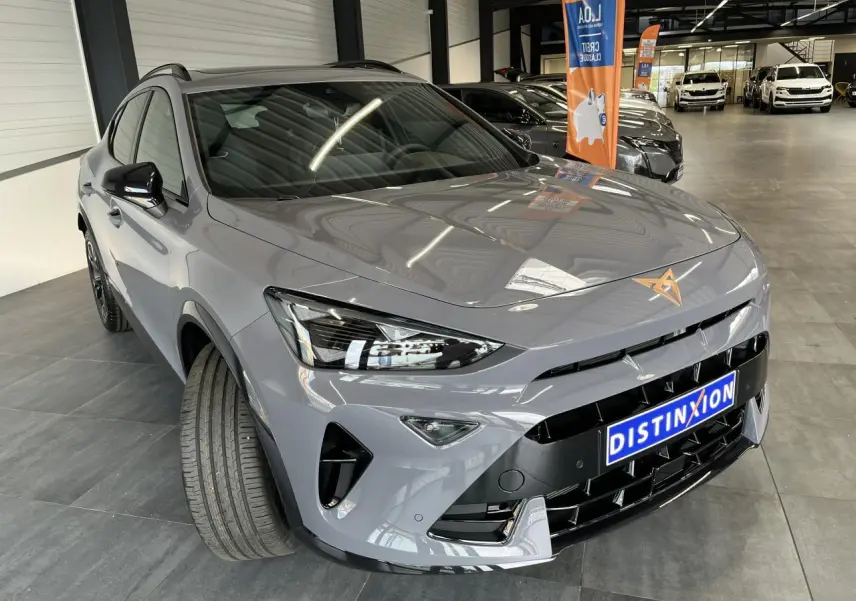 Vue 3/4 avant d'une CUPRA Formentor gris clair avec logo cuivré et calandre noire brillante en showroom.