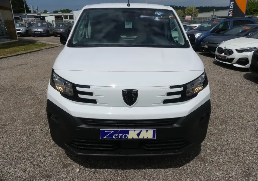 Vue frontale d'un Peugeot Partner blanc avec calandre noire et logo lion au centre, sur parking extérieur.