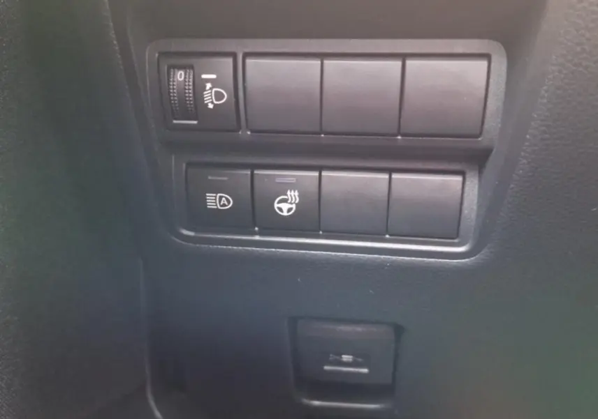 Gros plan sur les commandes de réglage des phares et du volant chauffant dans une Mazda2 hybride argentée de 2022.