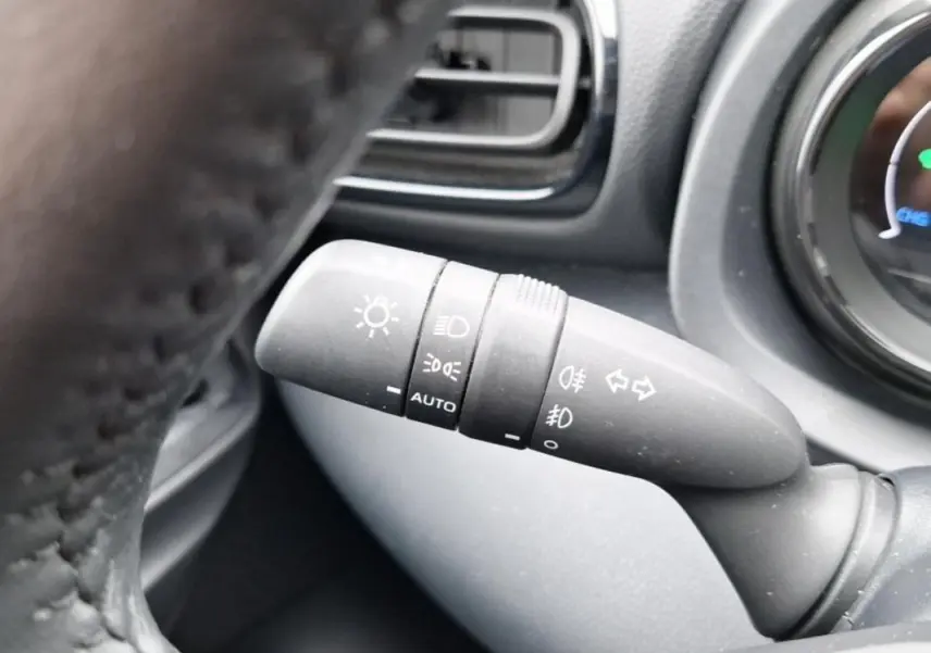 Commande des feux en gros plan à gauche du volant d'une Mazda2 hybride argent 2022, avec indication auto et phares antibrouillard.