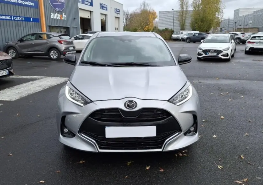 Vue frontale d'une Mazda2 Hybrid 2022 argent avec calandre noire et phares LED distinctifs sur un parking.