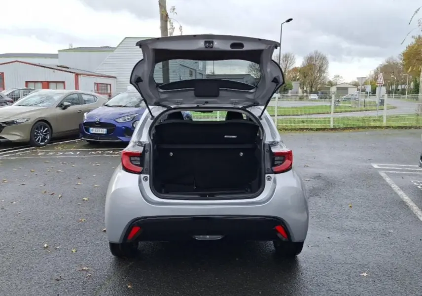 Vue arrière d'une Mazda2 hybride 2022 argent avec le coffre ouvert sur un parking extérieur.