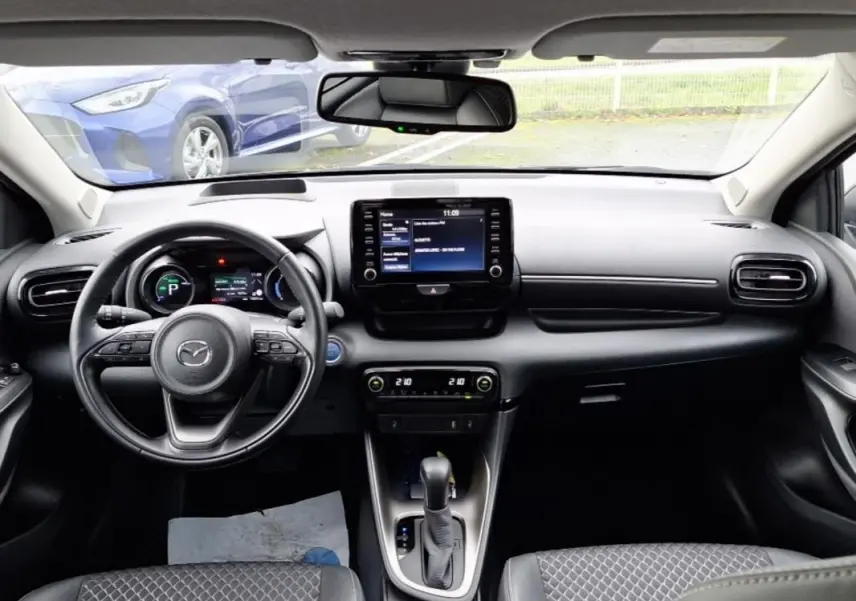 Vue intérieure avant de la Mazda2 hybride 2022, tableau de bord noir avec écran tactile et volant multifonction.