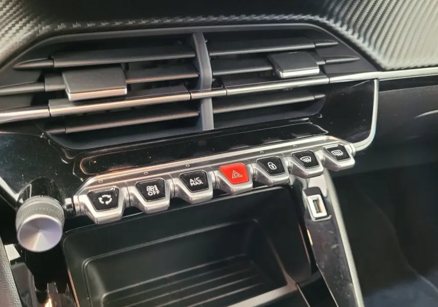 Gros plan sur la console centrale noire brillante de la Peugeot 208 2023 avec boutons de commande et aérateurs.