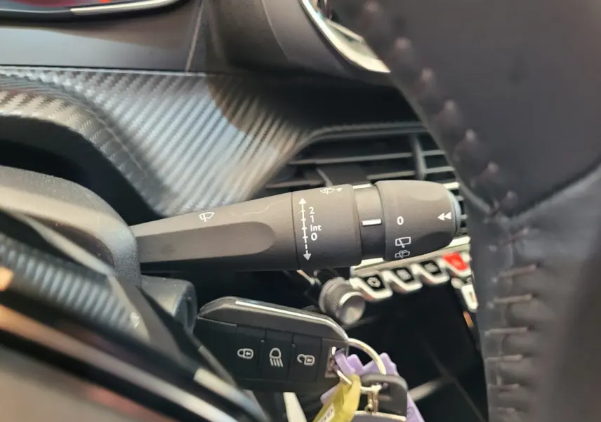 Gros plan sur la commande d’essuie-glace et clé de contact dans l’habitacle noir de la Peugeot 208 gris foncé 2023.