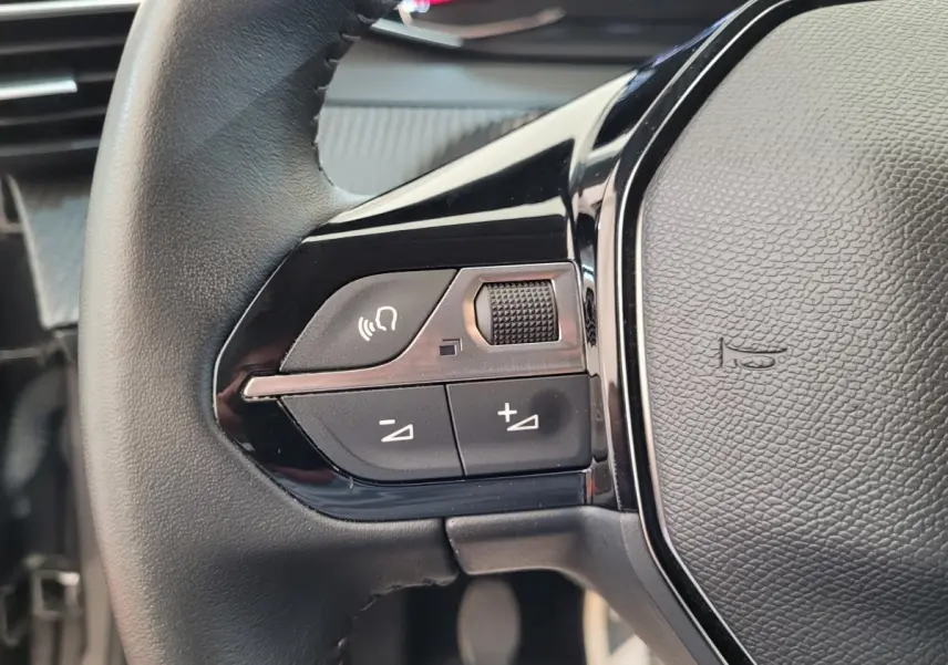 Gros plan sur la partie gauche du volant cuir de la Peugeot 208 gris foncé, avec commandes vocales et volume.