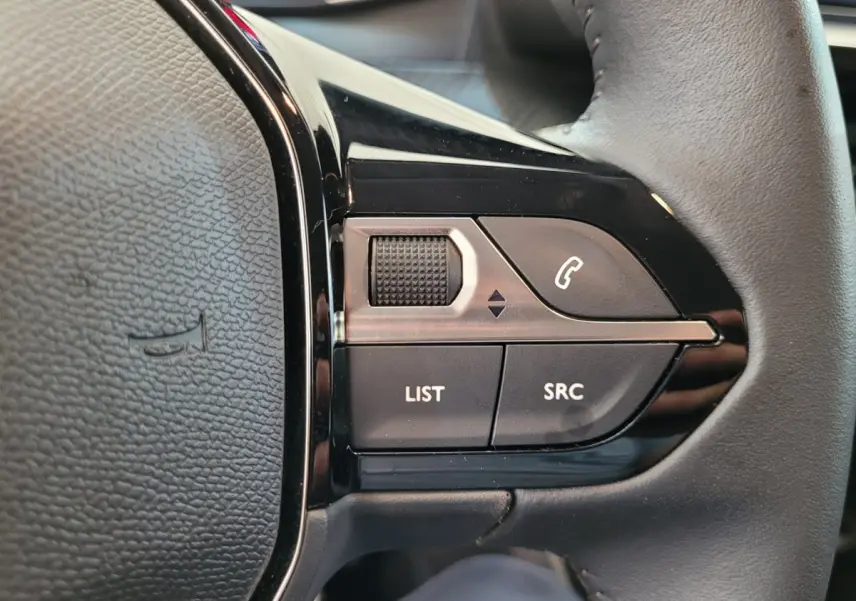 Gros plan sur les commandes gauche du volant cuir de la Peugeot 208 gris foncé, boutons LIST et SRC visibles.