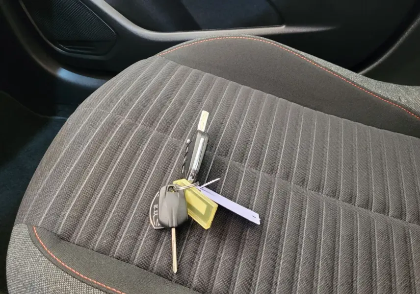 Clé de Peugeot 208 BlueHDi posée sur le siège avant tissu gris foncé avec surpiqûres rouges.