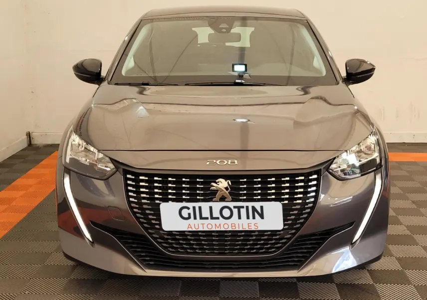 Vue frontale d'une Peugeot 208 gris foncé avec calandre noire et feux LED en forme de griffes lumineuses.