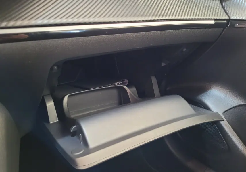 Gros plan sur la boîte à gants ouverte du Peugeot 208 gris foncé, montrant le tableau de bord et la finition intérieure.