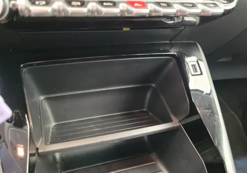 Rangement central ouvert avec port USB visible sur le côté dans l'habitacle d'une Peugeot 208 gris foncé.