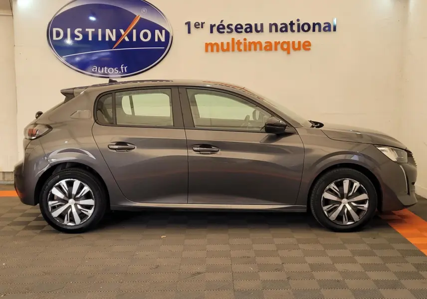 Profil côté droit d'une Peugeot 208 gris foncé 2023 garée en intérieur avec jantes alliage et rétroviseurs noirs.