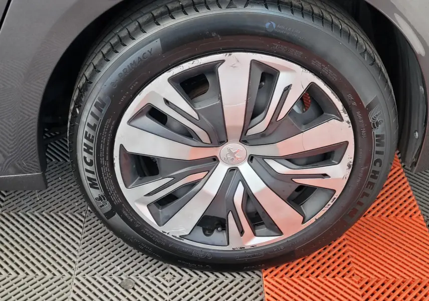 Gros plan sur la roue avant droite d'une Peugeot 208 gris foncé, mettant en valeur la jante et le pneu Michelin.