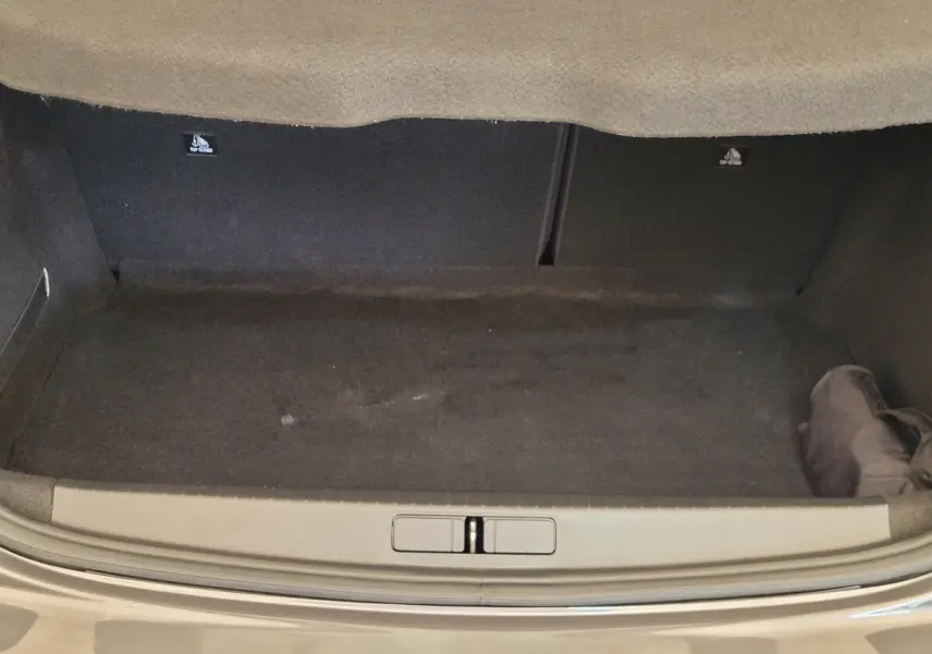 Coffre ouvert d'une Peugeot 208 gris foncé, vue de l'arrière montrant l'espace de chargement vide et la moquette noire.