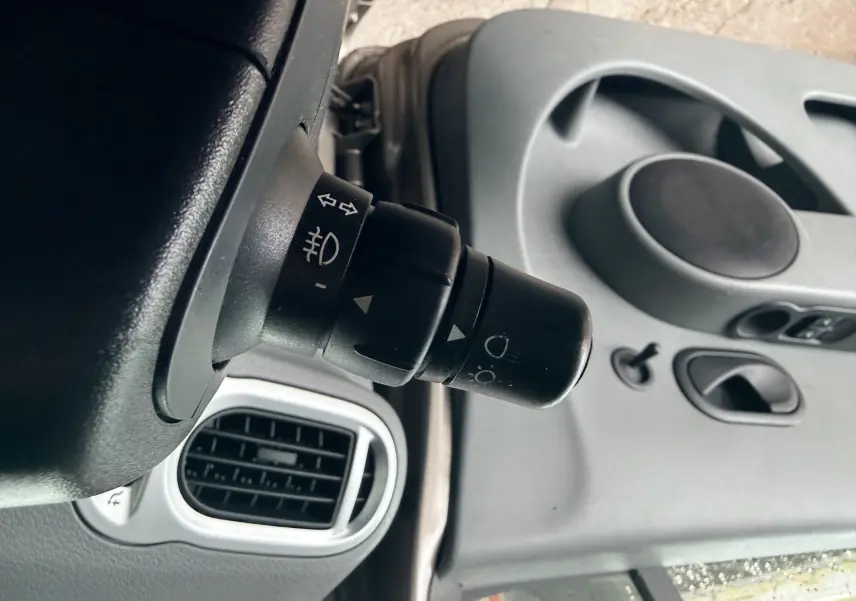 Gros plan sur la commande des phares et clignotants dans l'habitacle gris clair d'une Renault Modus beige.