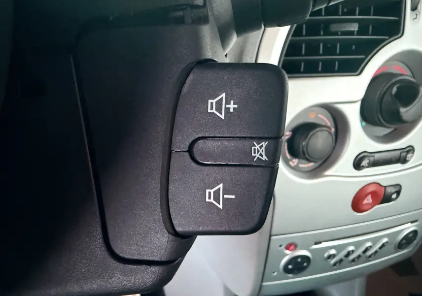 Gros plan sur les commandes de volume audio au volant d’une Renault Modus beige, tableau de bord gris en arrière-plan.