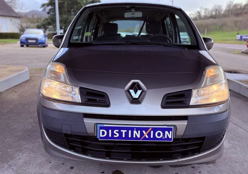 Vue avant d’une Renault Modus beige 2011 avec phares allumés et plaque d’immatriculation Distinxion visible.