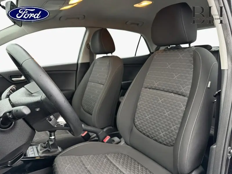 Vue intérieure côté conducteur de la KIA Rio 2018, sièges tissu Atlanta noirs avec volant cuir et levier de vitesse manuel.