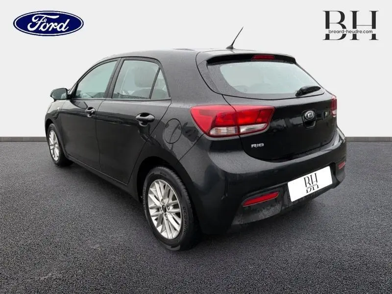 Vue 3/4 arrière droite d'une KIA Rio noire Ébène avec jantes alu et feux arrière rouges distinctifs.