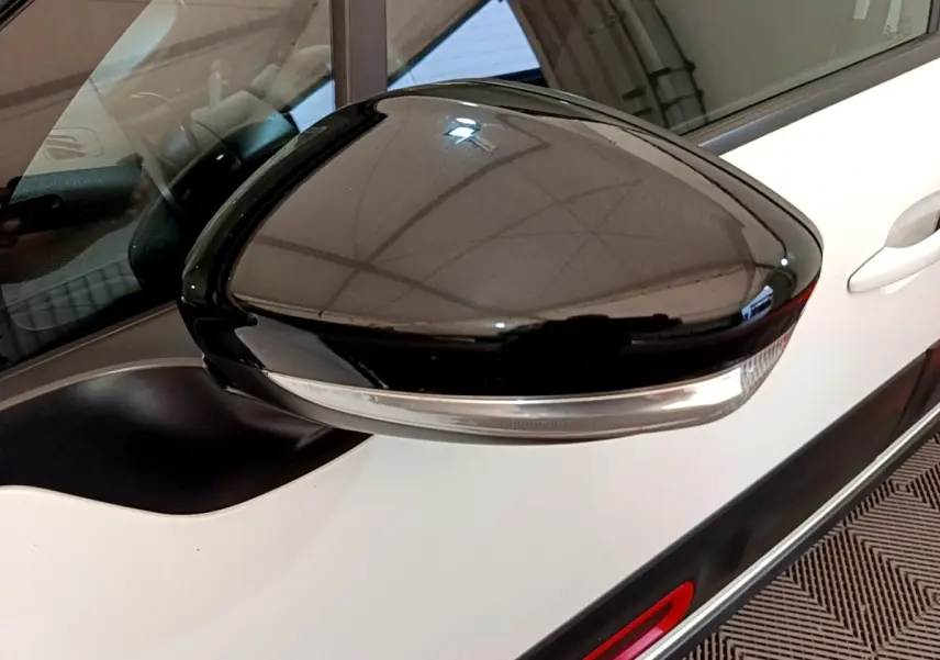 Gros plan sur le rétroviseur noir côté gauche d'une Citroën C3 blanche, avec partie de la portière visible.