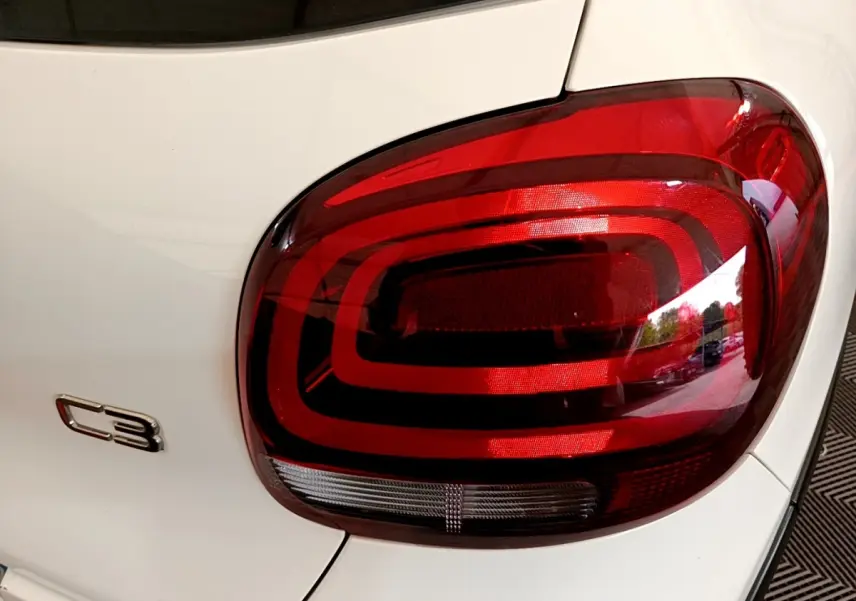 Gros plan sur le feu arrière droit rouge et le logo C3 sur la carrosserie blanche d'une Citroën C3 2021.