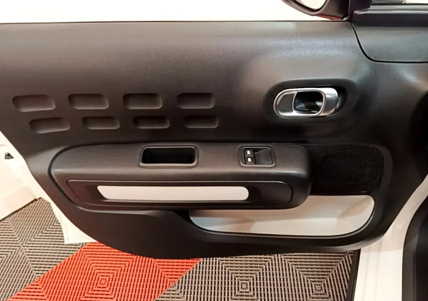 Vue rapprochée de la porte avant gauche blanche de la Citroën C3 avec poignée intérieure chromée et commandes de vitres.