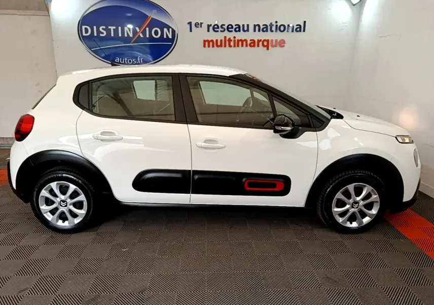 Profil droit d'une Citroën C3 blanche 2021 avec protections latérales noires et insert rouge, en intérieur showroom.