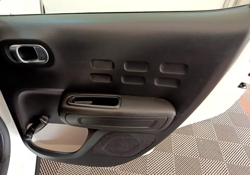 Vue rapprochée de la porte avant gauche noire avec poignée et manivelle sur une Citroën C3 blanche.