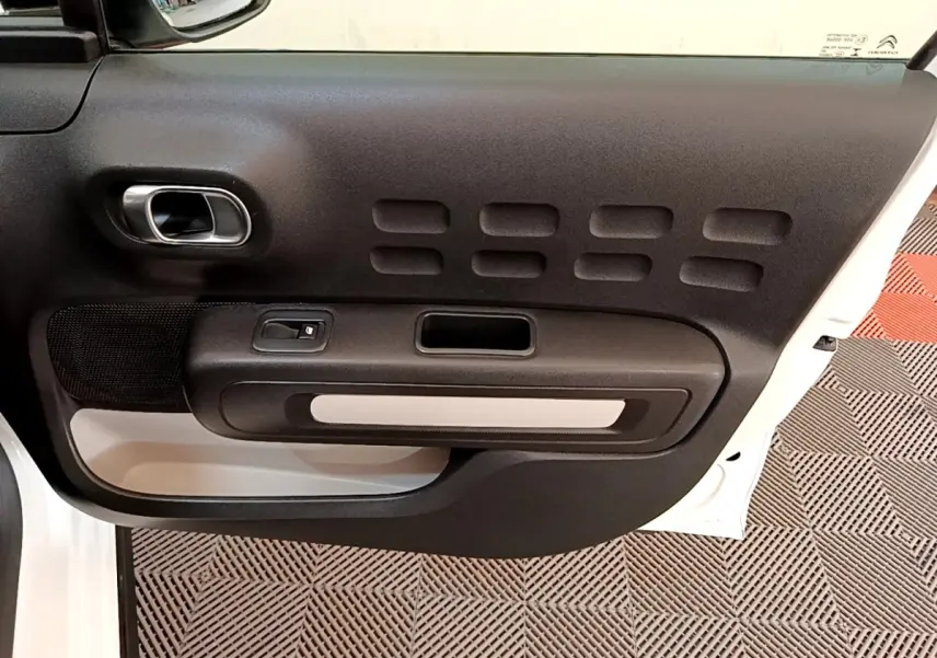 Vue intérieure de la porte côté gauche blanche d'une Citroën C3 2021 avec poignée argentée et panneau noir texturé.