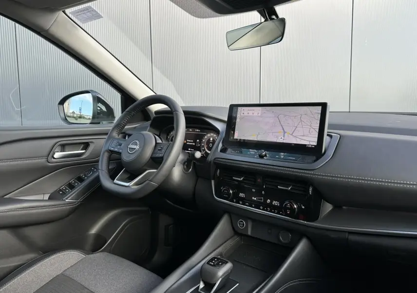 Vue intérieure côté conducteur du Nissan Qashqai 2025, tableau de bord noir avec écran tactile de navigation et volant cuir.