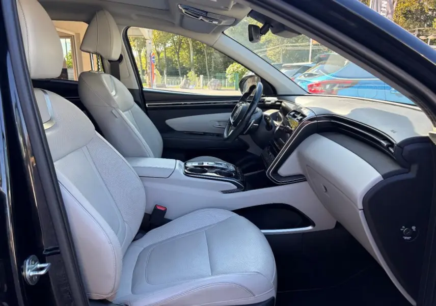 Vue intérieure côté conducteur du Hyundai Tucson noir 2022, sièges clairs et console centrale avec volant cuir.