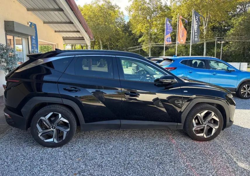 Hyundai Tucson noir vu de profil côté gauche, avec jantes alliage et barres de toit visibles en extérieur.