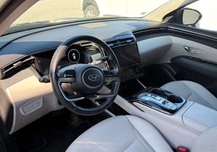 Vue intérieure côté conducteur du Hyundai Tucson 2022, volant cuir, sièges clairs et console centrale avec écran tactile.