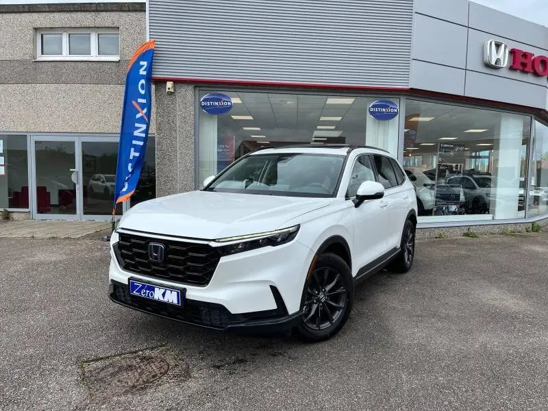 Honda CR-V blanc platine nacrée vu en 3/4 avant droit devant une concession Honda avec jantes noires.