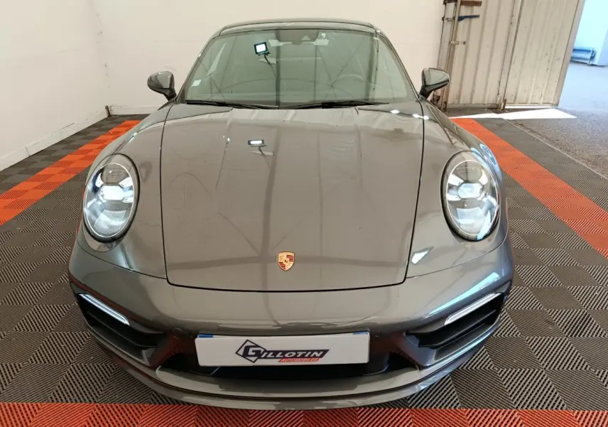 Vue avant d'une Porsche 911 Carrera 4S Coupé gris foncé, avec phares ronds LED et logo Porsche visible sur le capot.