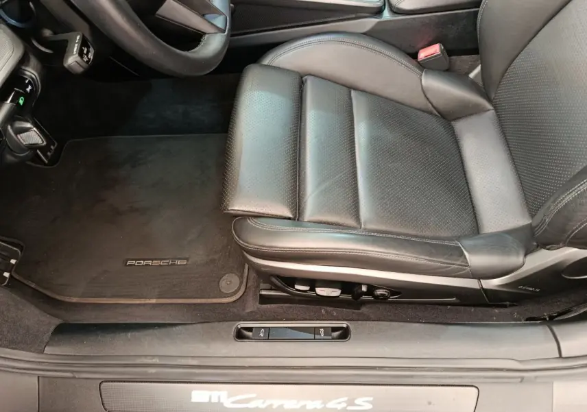 Vue rapprochée du siège conducteur en cuir noir et tapis de sol Porsche d'une 911 Carrera 4S Coupé gris foncé.