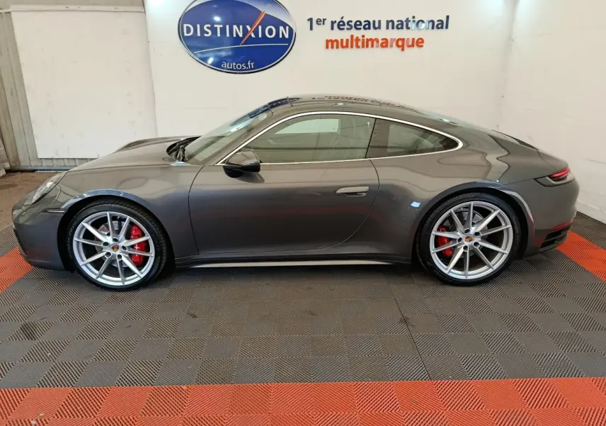 Profil droit d'une Porsche 911 Carrera 4S Coupé gris foncé avec jantes argentées et étriers de frein rouges, en intérieur showroom.
