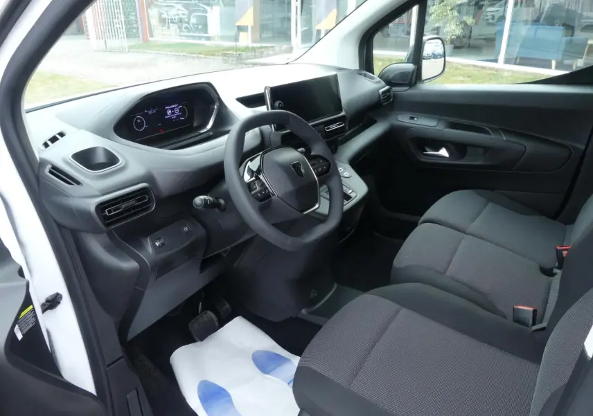 Intérieur côté conducteur du Peugeot Partner blanc 2025, avec tableau de bord moderne et sièges tissu gris.