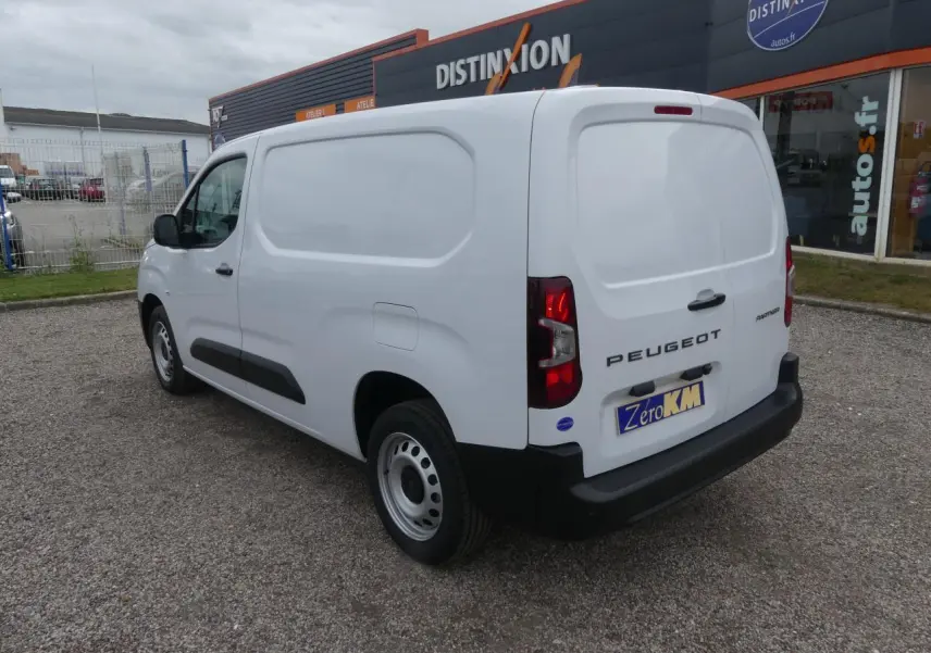 Vue 3/4 arrière droite d'un Peugeot Partner blanc avec portes arrière battantes et jantes tôle grises sur parking.