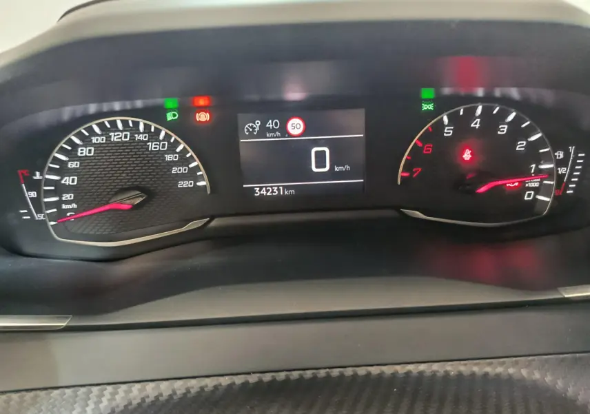 Vue rapprochée du tableau de bord numérique de la Peugeot 208 blanche, affichant vitesse et compte-tours.